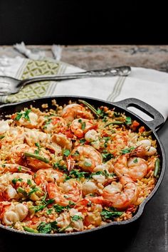 a skillet filled with shrimp and rice on top of a table next to a fork