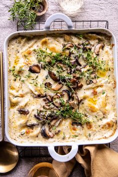 a casserole dish with mushrooms and herbs in it on a table next to spoons