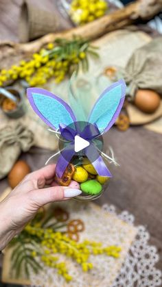 a person holding an origami easter bunny in their hand with eggs and flowers on the table