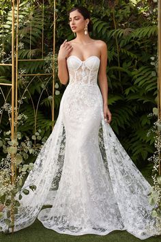 a woman in a white wedding dress standing next to a gold trellis and greenery