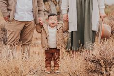 a little boy holding the hands of his parents while they walk through some tall grass