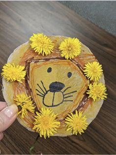 someone is holding up a paper plate with a lion face and yellow flowers on it