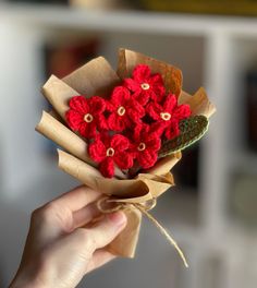 a hand holding a bouquet of red crocheted flowers in brown paper wrappers