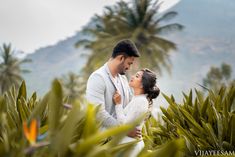 a man and woman standing next to each other in front of palm trees with mountains in the background