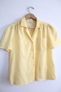 "Cute yellow and white vertical striped button down blouse from the 80s. It has a chest pocket and gathering around the shoulder and sleeve. Good condition besides a small burn hole at the front. 'Rhoda Lee' brand Feels like Polyester and fits like a size L Measurements are: 22\" long 9\" long sleeves 19\" wide 2.5\" collar S-1" Summer Vertical Stripes Button-up Blouse, Yellow Summer Blouse With Pockets, Striped Tops With Pockets For Daywear, Yellow Blouse With Pockets For Summer, Vintage Tops With Pockets For Spring, Vintage Relaxed Fit Blouse With Pockets, Vintage Blouse With Pockets In Relaxed Fit, Vintage Blouse With Pockets Relaxed Fit, Vintage Blouse With Pockets And Relaxed Fit