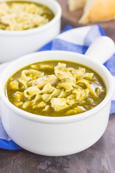 two white bowls filled with soup on top of a wooden table next to bread and blue napkin