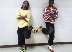 two young men standing next to each other in front of a wall