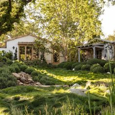 the house is surrounded by lush green grass and rocks, with trees in the background