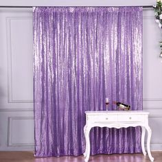 a white table sitting next to a purple curtain on top of a wooden floor in front of a wall