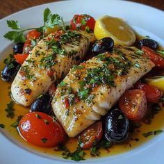 two fish fillets on a plate with tomatoes, olives and lemon