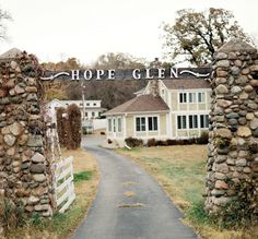 the entrance to hope glen is surrounded by stone pillars and gated in grass, with a white house behind it