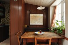 a wooden table with two chairs and a bowl of fruit on it in front of a window