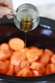 a person pouring oil into a slow cooker filled with carrots