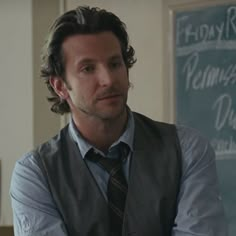 a man wearing a vest and tie standing in front of a chalkboard