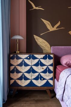 a blue and white cabinet sitting in front of a bed next to a wall with birds painted on it