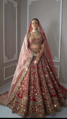 a woman in a red and gold bridal gown standing next to a white wall