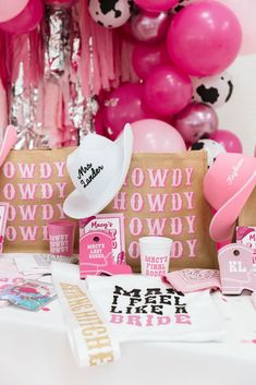 a table topped with pink and white balloons, paper bags and other items for a cowgirl birthday party