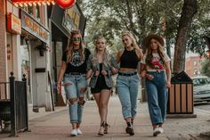 three girls walking down the sidewalk in front of a neon sign