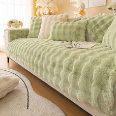 a living room with a couch covered in fluffy green blankets and pillows on the floor