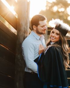 a man and woman standing next to each other near a fence wearing graduation gowns