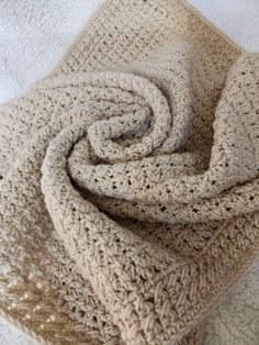 a crocheted blanket laying on top of a white bed sheet with a knot at the end