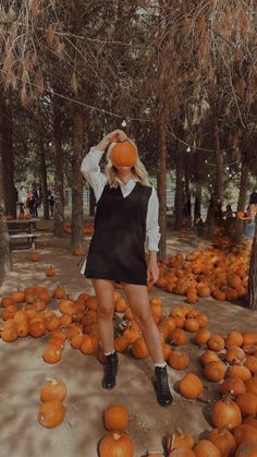 a woman in a black dress and hat standing among pumpkins at a pumpkin patch