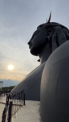 the sun is setting behind a large statue