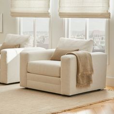 a living room with two white chairs and a beige rug in front of the windows