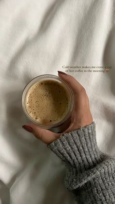 a woman's hand holding a cup of coffee on top of a white sheet