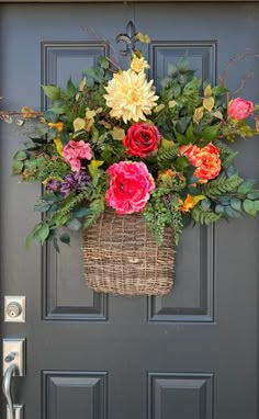 a basket filled with flowers hanging from the side of a gray door next to a black front door