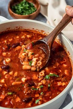 a wooden spoon in a white bowl filled with chili and pasta soup on a table