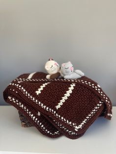 two small knitted animals sitting on top of a brown and white blanket with stripes