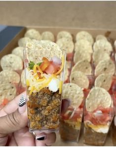 a person holding up a glass with food in it next to some tortilla shells