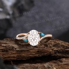 an oval cut diamond ring with turquoise stones in the band on top of a piece of wood