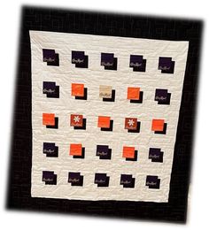 a white and black quilt with orange squares on the bottom, along with words written in gold