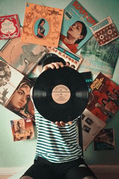 a person sitting on the floor holding up a record in front of a wall full of records