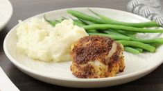 a white plate topped with chicken and mashed potatoes next to green beans on a table