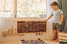 a young boy standing in front of a toy truck on top of a wooden shelf