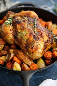 a close up of a chicken in a pan with potatoes and carrots on the side