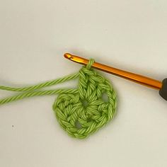 an orange crochet hook is next to a green knitted object on a white surface