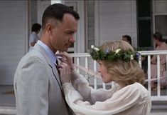 a man adjusting the collar of a woman's dress in front of a house