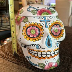 a white sugar skull with colorful flowers and a cross on it's forehead sits next to a measuring tape