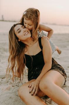 a mother and her daughter playing in the sand at the beach with their arms around each other