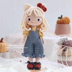 a crocheted doll standing on top of a table next to small pumpkins