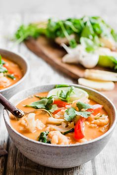 two bowls filled with soup and vegetables on top of a wooden table next to a cutting board