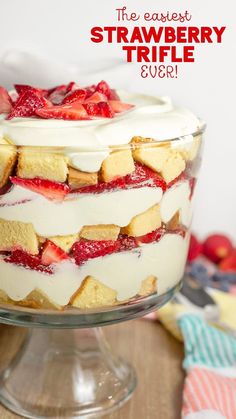 a layered trifle with strawberries and cream in a glass dish on a wooden table