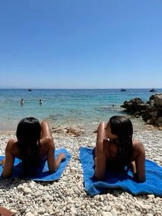 two women are sitting on towels at the beach