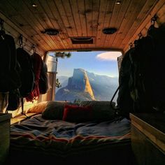 the inside of a van with mountains in the background and a bed on the floor