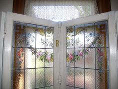 two glass doors with flowers painted on them in front of a window sill and curtain