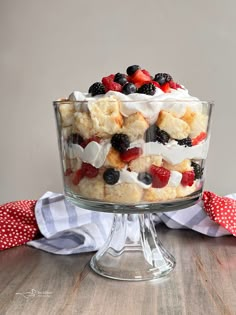 a trifle with berries, cream and blueberries in a glass dish on a wooden table